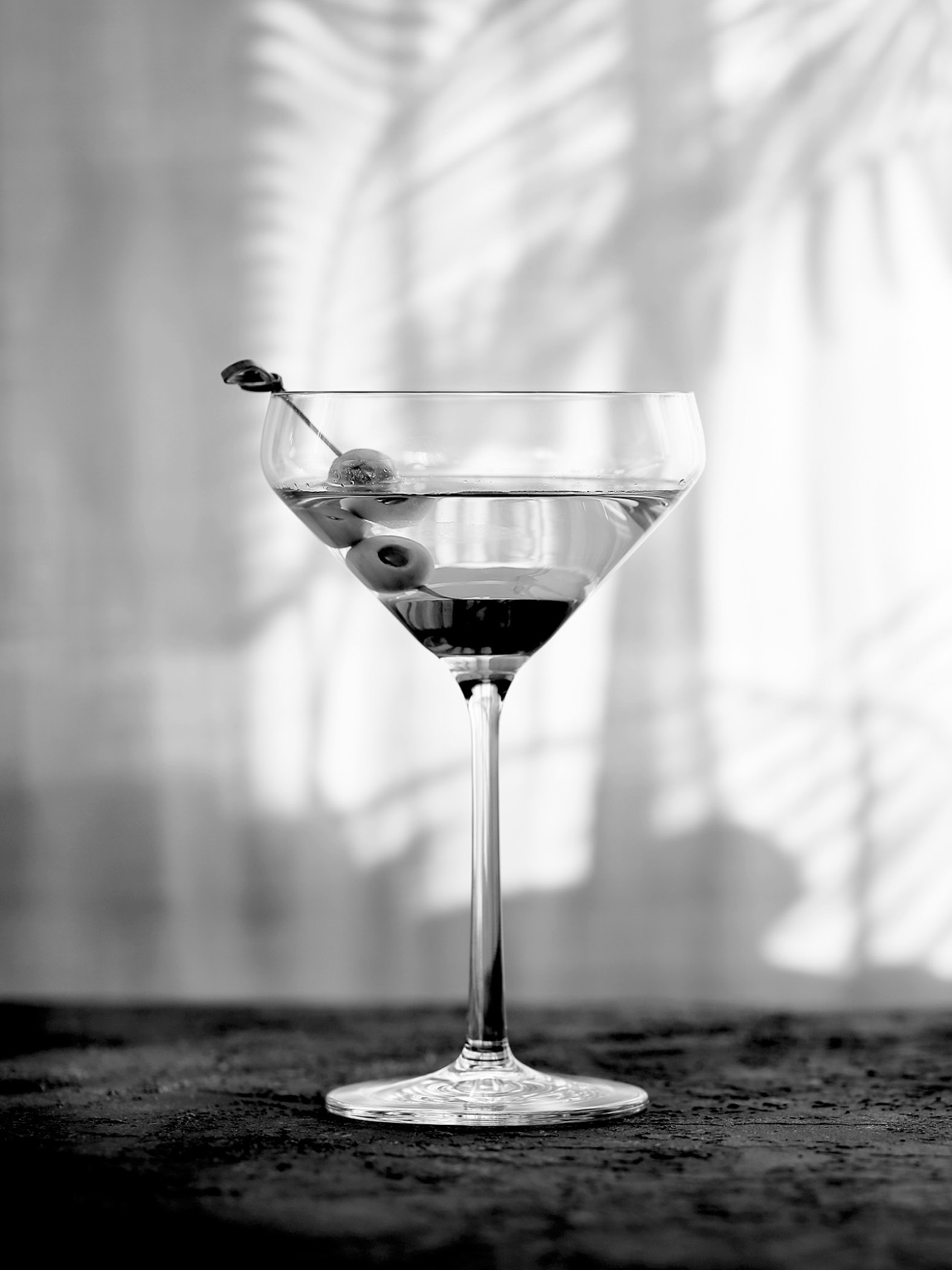 Cocktailglas mit Oliven auf dunklem Untergrund, Schatten im Hintergrund