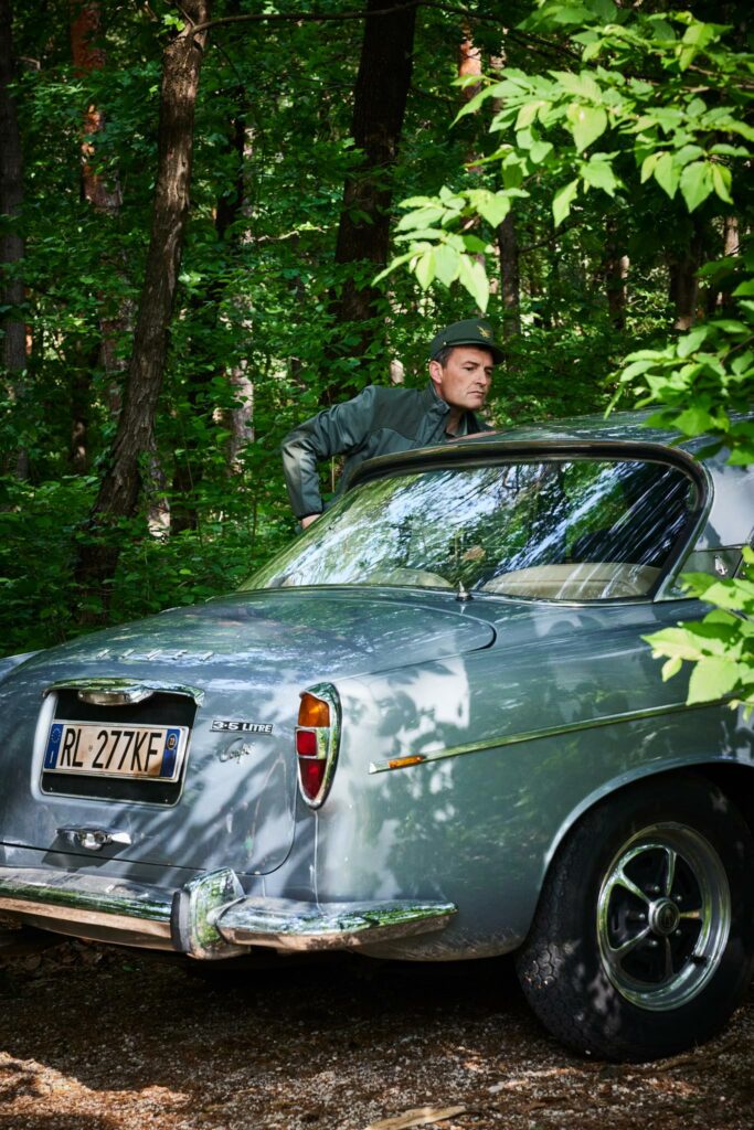Mann neben klassischem Auto im schattigen Wald